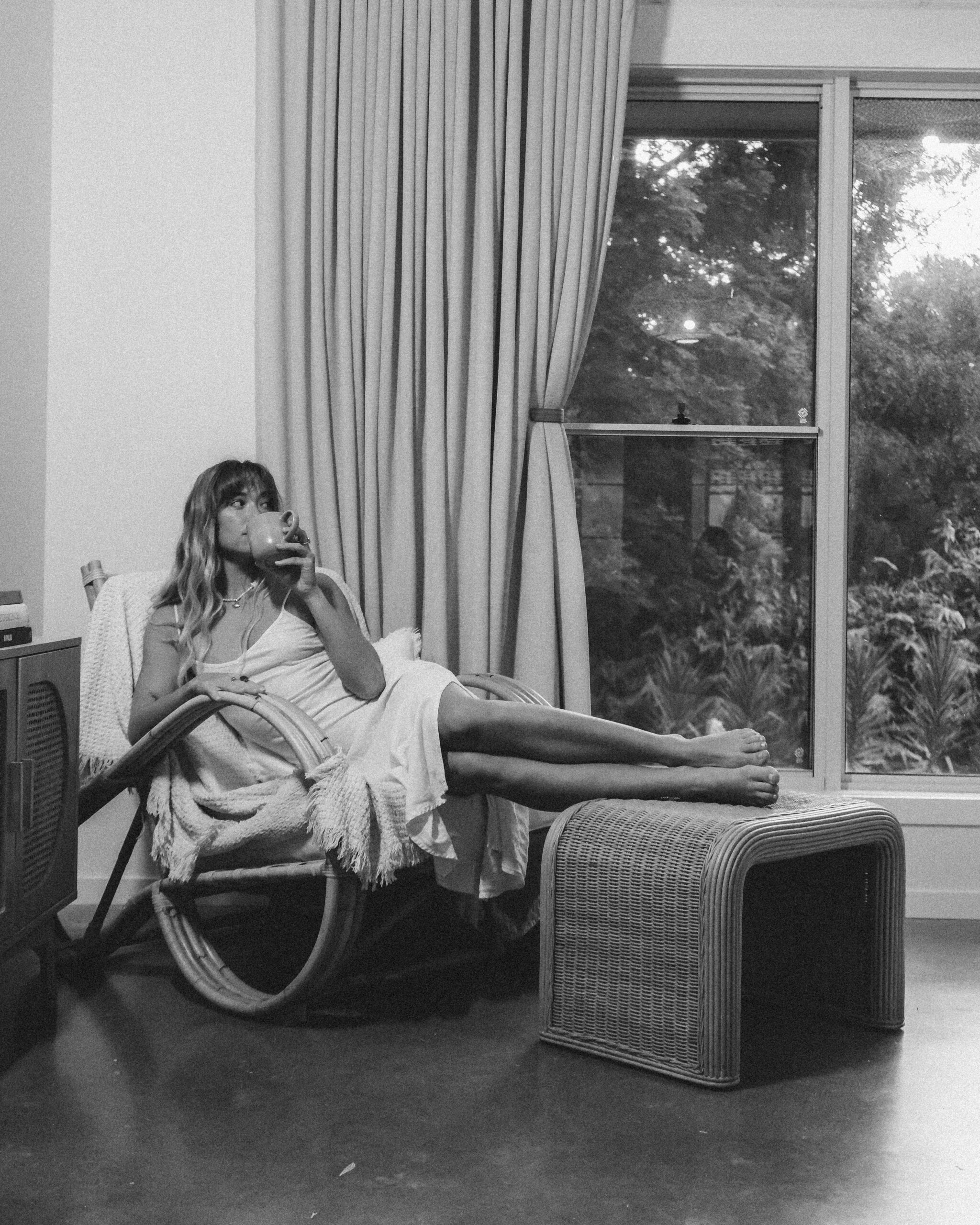Monochrome image of a woman sipping from a cup, seated by a window at a luxury villa in Ewingsdale.